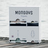 A stainless steel menstrual product dispenser in white with the brand name 'Mondays Organic' on the front, placed on a wooden surface with water in the background.