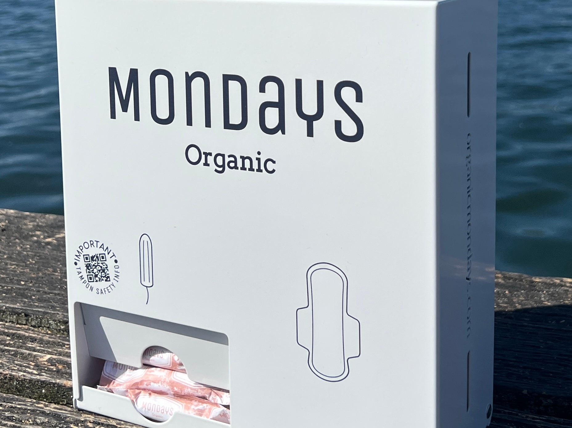 A white free-vend Mondays dispenser for  the provision of organic pads & digital (non applicator) tampons in workplaces, schools and sportsvenues