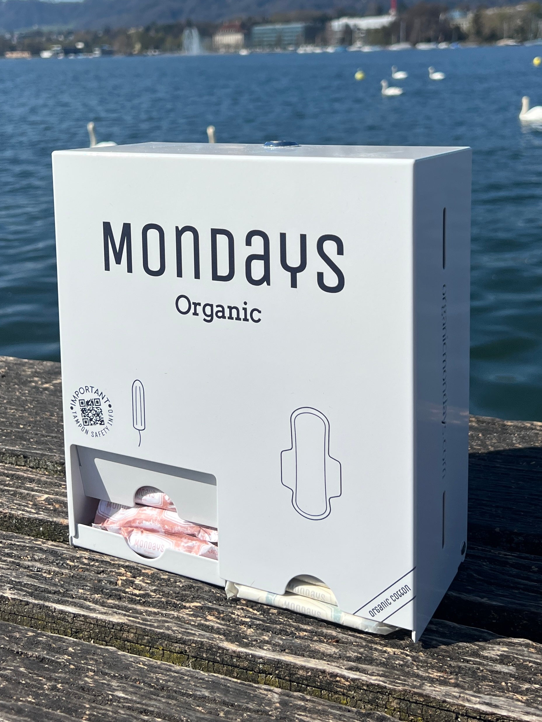 A white free-vend Mondays dispenser for  the provision of organic pads & digital (non applicator) tampons in workplaces, schools and sportsvenues