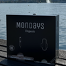 Mondays Organic BLACK dispenser for organic sanitary pads and applicator tampons sitting on a wooden surface with a lake and mountains in the background